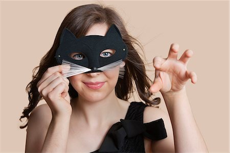 Portrait of a young woman looking through eye mask imitating as cat over colored background Stock Photo - Premium Royalty-Free, Code: 693-06121432
