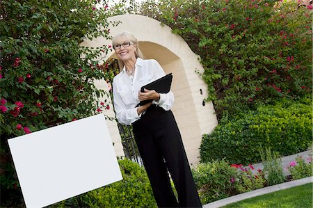 realtor woman - Tilt shot of cheerful senior agent standing by sign board with clipboard Stock Photo - Premium Royalty-Free, Code: 693-06324011