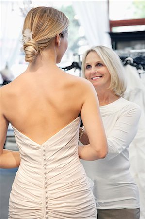 fashion for older women - Back view of woman dressed in bridal gown with happy senior owner assisting Stock Photo - Premium Royalty-Free, Code: 693-06324055