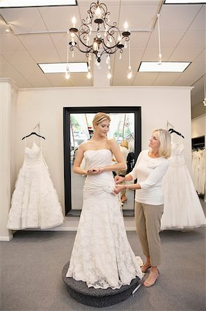 Beautiful woman dressed up as bride with senior employee helping in bridal store Stock Photo - Premium Royalty-Free, Code: 693-06324056