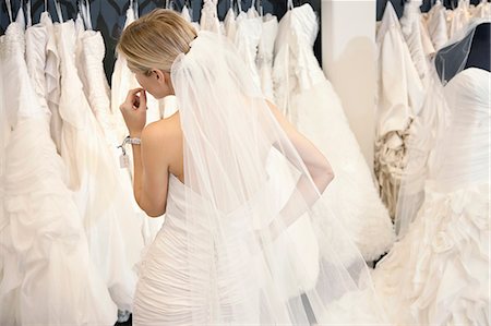 simsearch:693-06325150,k - Back view of a young woman in wedding dress looking at bridal gowns on display in boutique Stock Photo - Premium Royalty-Free, Code: 693-06324075