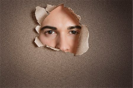 Portrait of a young Caucasian man peeking from ripped paper hole Stock Photo - Premium Royalty-Free, Code: 693-06324085