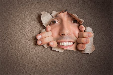 rasgar - Portrait of a happy young Hispanic man peeking from ripped paper hole Foto de stock - Sin royalties Premium, Código: 693-06324088