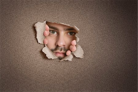 picture of a man peeking - Portrait of a mid adult Caucasian man peeking from ripped paper hole Stock Photo - Premium Royalty-Free, Code: 693-06324083