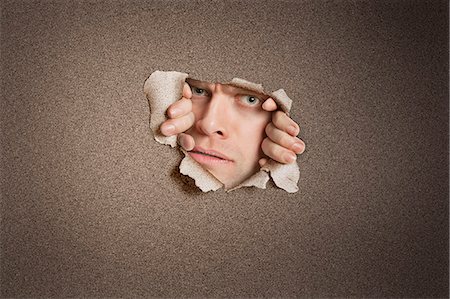 simsearch:693-06324094,k - Portrait of a mid adult Caucasian man peeking from ripped white paper hole Stock Photo - Premium Royalty-Free, Code: 693-06324093