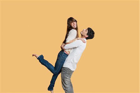 stood - Happy young man carrying girlfriend over colored background Stock Photo - Premium Royalty-Free, Code: 693-06324137