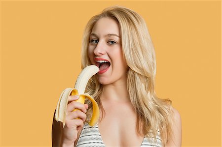 people with fruits cutout - Portrait of a beautiful blond woman eating banana over colored background Foto de stock - Sin royalties Premium, Código: 693-06324131