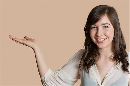 Portrait of a happy young woman with empty hand over colored background Stock Photo - Premium Royalty-Free, Code: 693-06324172