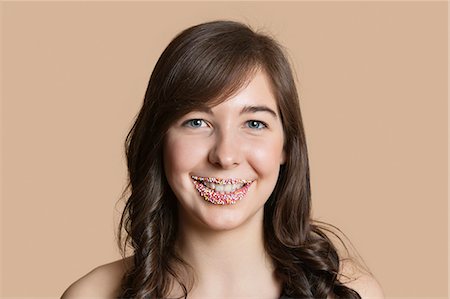 Portrait of a happy young woman with sprinkled lips over colored background Stock Photo - Premium Royalty-Free, Code: 693-06324207