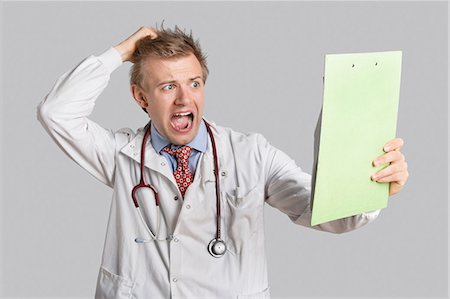 Male doctor terrified looking at medical reports over gray background Stock Photo - Premium Royalty-Free, Code: 693-06324213