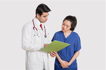 Doctor discussing medical report with female nurse over gray background Stock Photo - Premium Royalty-Free, Code: 693-06324235