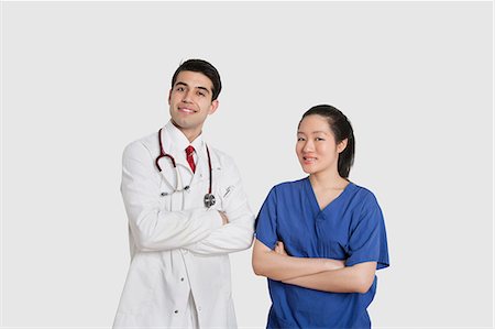 simsearch:693-06324255,k - Portrait of male doctor and female nurse standing with hands folded over gray background Foto de stock - Royalty Free Premium, Número: 693-06324236