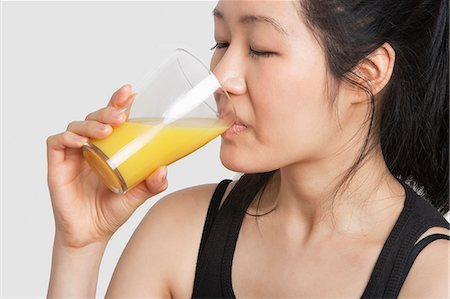 succo d'arancia - Young woman drinking orange juice over gray background Fotografie stock - Premium Royalty-Free, Codice: 693-06324267