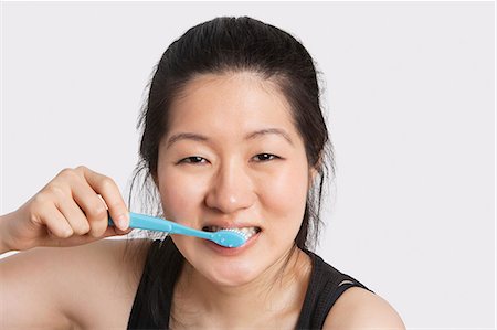simsearch:693-06324350,k - Portrait d'une jeune femme se brosser ses dents sur fond gris clair Photographie de stock - Premium Libres de Droits, Code: 693-06324269