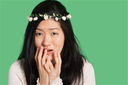 Portrait of a young woman expressing fear and anxiety over green background Stock Photo - Premium Royalty-Free, Code: 693-06324277