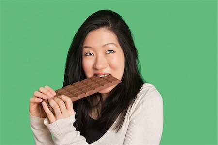 eating indulgent chocolate - Cute young woman eating a large chocolate bar over green background Stock Photo - Premium Royalty-Free, Code: 693-06324280