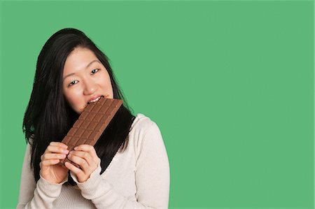 sweet (taste) - Portrait of a young woman eating a large chocolate bar over green background Stock Photo - Premium Royalty-Free, Code: 693-06324281