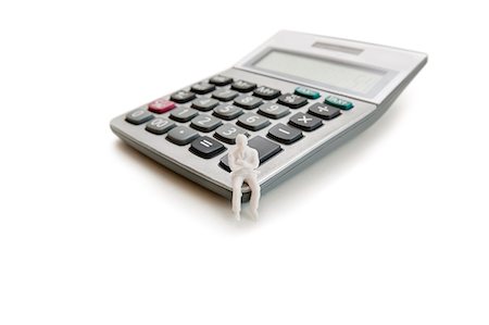 A small dummy figure sitting on a calculator over white background Fotografie stock - Premium Royalty-Free, Codice: 693-06324344