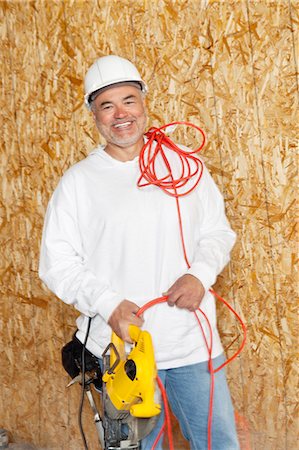 Portrait of a happy male construction worker holding a power saw and a red electric wire Stock Photo - Premium Royalty-Free, Code: 693-06324514