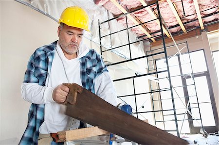 Serious male construction worker cutting wood with handsaw Foto de stock - Sin royalties Premium, Código: 693-06324517