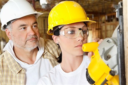 Female worker cutting wood with a power saw while male worker standing behind Foto de stock - Sin royalties Premium, Código: 693-06324511