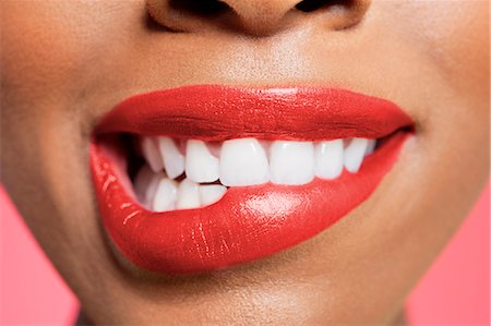 Close-up view of an female biting her red lip over colored background Stock Photo - Premium Royalty-Free, Code: 693-06324638