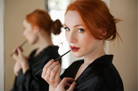 Portrait of a redheaded woman applying lip liner Stock Photo - Premium Royalty-Free, Code: 693-06324739