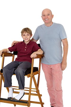 preteen boy happy white background - Portrait of senior man with pre-teen boy sitting on director's chair over white background Stock Photo - Premium Royalty-Free, Code: 693-06324814