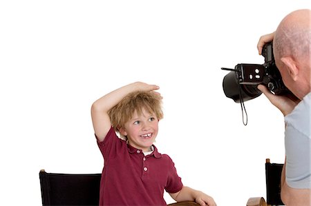 simsearch:693-06324785,k - Senior photographer clicking school kid sitting on chair over white background Stock Photo - Premium Royalty-Free, Code: 693-06324817