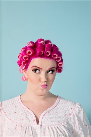 Young woman making faces with pink hair and curlers over colored background Stock Photo - Premium Royalty-Free, Code: 693-06323940