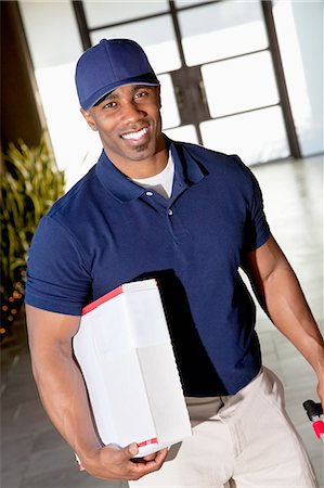 Tilt image of a happy African American delivery man looking at camera Stock Photo - Premium Royalty-Free, Code: 693-06323979