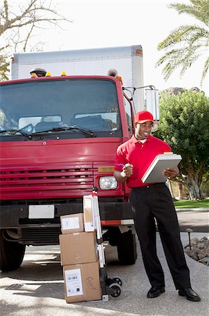 simsearch:693-06323989,k - Young delivery man looking at delivery list on clipboard with truck in background Foto de stock - Sin royalties Premium, Código: 693-06323988