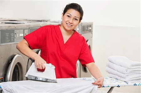 ferro de passar roupas - Portrait of a happy woman employee in red uniform ironing clothes in Laundromat Foto de stock - Royalty Free Premium, Número: 693-06323999