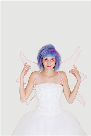 simsearch:693-06379524,k - Portrait of happy young woman dressed as angel with dyed hair against gray background Foto de stock - Royalty Free Premium, Número: 693-06378811