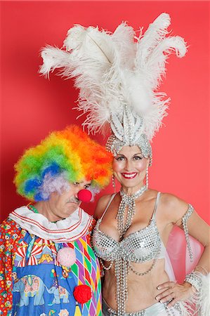 Portrait de joyeux showgirl senior avec clown triste permanent sur fond rouge Photographie de stock - Premium Libres de Droits, Code: 693-06378837