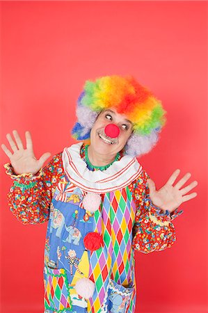 Clown drôle avec armes soulevées à la recherche de suite contre le fond coloré Photographie de stock - Premium Libres de Droits, Code: 693-06378849