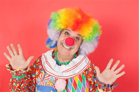 Portrait of funny clown with arms raised against colored background Fotografie stock - Premium Royalty-Free, Codice: 693-06378850