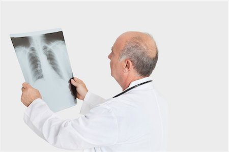 simsearch:693-06378921,k - Senior male doctor examining medical radiograph over gray background Foto de stock - Sin royalties Premium, Código: 693-06378909