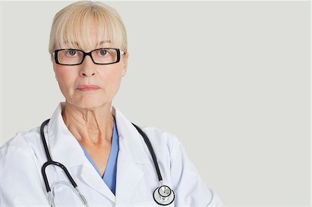 female doctor serious - Portrait of serious female doctor with stethoscope around neck over gray background Stock Photo - Premium Royalty-Free, Code: 693-06378919