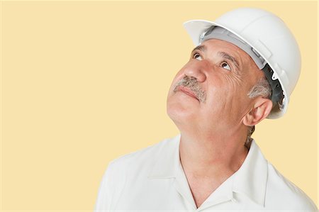 simsearch:693-06379322,k - Senior construction worker with hardhat looking up over yellow background Foto de stock - Sin royalties Premium, Código: 693-06378930