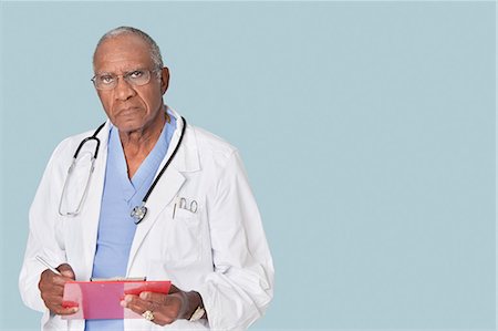 simsearch:693-06379058,k - Portrait of an African American senior doctor holding clipboard over light blue background Foto de stock - Sin royalties Premium, Código: 693-06379049