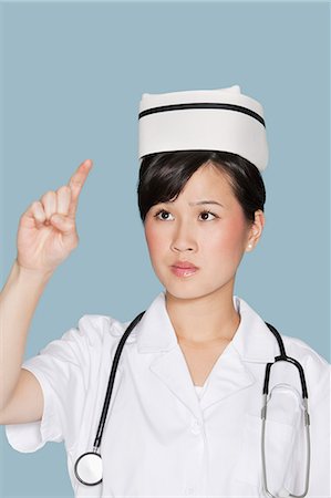 Young nurse using transparent screen over light blue background Stock Photo - Premium Royalty-Free, Code: 693-06379040