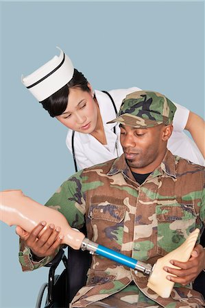 simsearch:693-06379155,k - Nurse with soldier holding artificial limb as he sits in wheelchair, studio shot on light blue background Stock Photo - Premium Royalty-Free, Code: 693-06379042