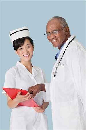 Portrait of happy medical professionals having a discussion over medical report against light blue background Stock Photo - Premium Royalty-Free, Code: 693-06379055