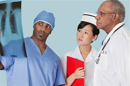 female doctor cap - Multi ethnic doctors examining x-ray report over light blue background Stock Photo - Premium Royalty-Free, Code: 693-06379056