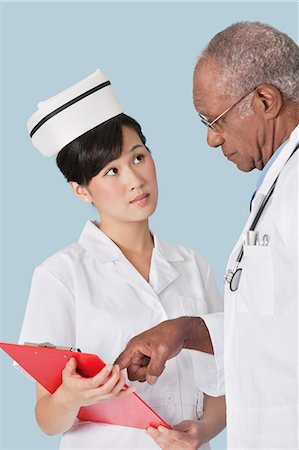 senior asian male doctor with stethoscope - Two medical professionals having a discussion over medical report against light blue background Stock Photo - Premium Royalty-Free, Code: 693-06379053