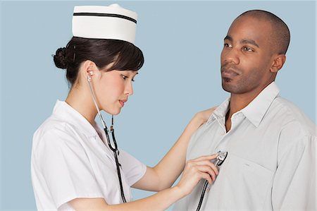 Female doctor listening the heartbeat of male patient over light blue background Stock Photo - Premium Royalty-Free, Code: 693-06379066
