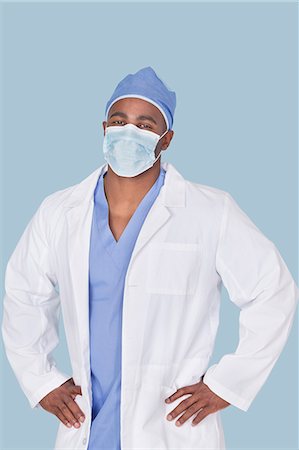 portrait of man in lab coat - Portrait of an African American male surgeon with hands on hips over light blue background Stock Photo - Premium Royalty-Free, Code: 693-06379074