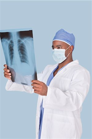 Male doctor analyzing x-ray report over light blue background Stock Photo - Premium Royalty-Free, Code: 693-06379073