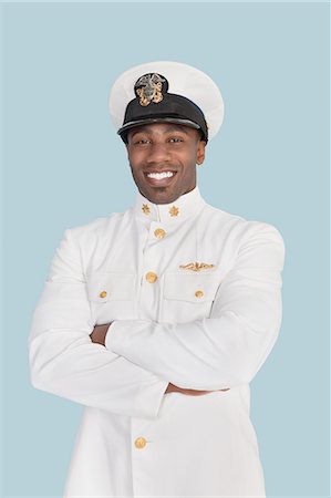 Portrait d'un jeune officier de marine américaine heureux debout avec les bras croisés sur fond bleu clair Photographie de stock - Premium Libres de Droits, Code: 693-06379104